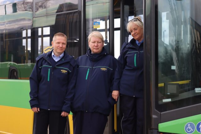 Troje pracowników w granatowych kurtkach przy autobusie