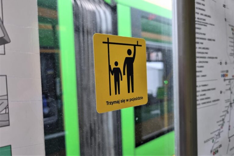 Piktogram naklejony na szybie tramwaju. Na żółtym tle czarne postaci trzymające się uchwytów
