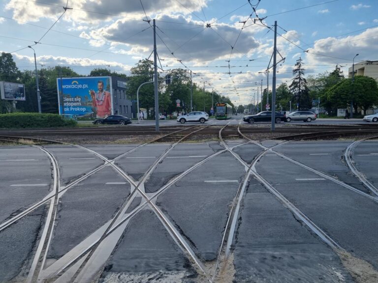 Zniszczone łuki torowiska - widok na skrzyżowanie. Na wprost, w tle, tramwaj