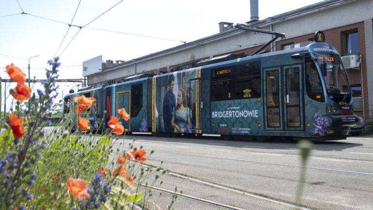 Oklejony reklamą tramwaj na tle kwitnących roślin