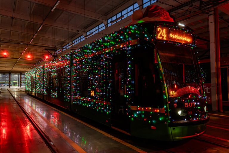 Rozświetlony lampkami tramwaj z czapką świętego Mikołaja nad kabiną motorniczego w oświetlonej na czerwono hali