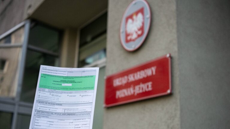 Trzymany w ręku formularz PIT na tle budynku urzędu skarbowego
