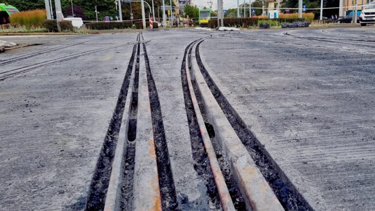 Nawierzchnia z czarnego betonu przy torowisku. W tle tramwaj