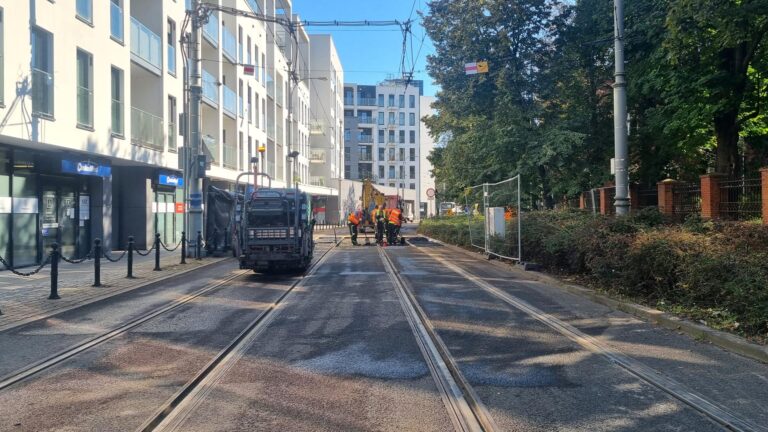 Asfaltowanie nawierzchni. W tle pracownicy w pomarańczowych odblaskowych kamizelkach