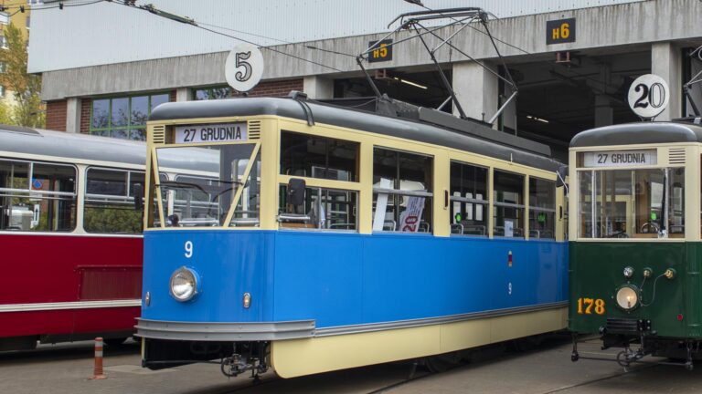 Niebieski tramwaj ustawiony centralnie, po bokach wagony w innych kolorach