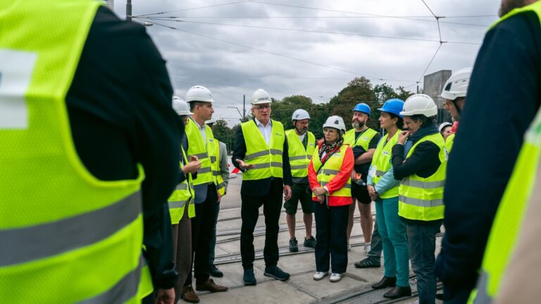 Osoby w odblaskowych kamizelkach rozmawiają na placu budowy
